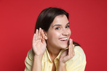 Woman showing hand to ear gesture on red background