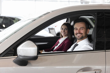 Fototapeta premium Happy saleswoman and client inside new car in salon
