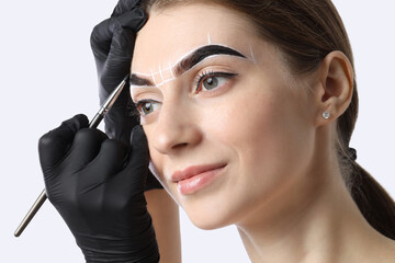 Obraz premium Young woman undergoing henna eyebrows dyeing procedure on light background, closeup