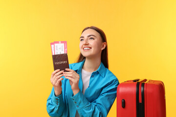 Woman with tickets, passport and suitcase on orange background