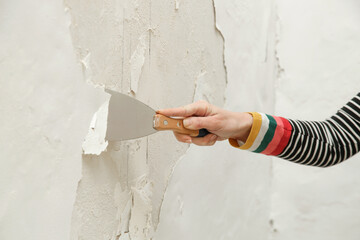 Saltpeter or mold on the wall problem. Woman is using a scraper to scrape and remove all loose...