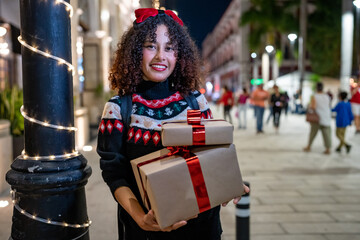 Young woman holding christmas gifts on a decorated street at night