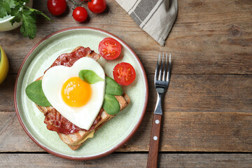 Tasty sandwich with heart shaped fried egg and bacon on wooden table, flat lay. Space for text