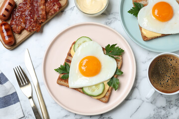 Tasty sandwiches with heart shaped fried eggs for romantic breakfast on white marble table, flat lay