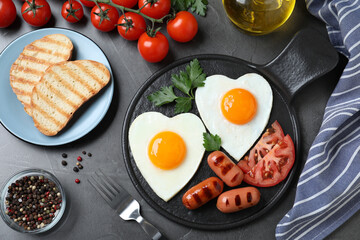 Delicious breakfast with heart shaped fried eggs and  sausages served on dark grey table, flat lay