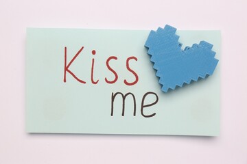 Card with phrase Kiss me and blue heart on white background, top view