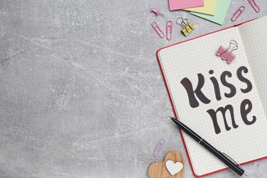 Phrase Kiss me written in notebook and stationery on light grey stone table, flat lay. Space for text