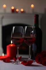 Romantic table setting with glasses of red wine, burning candles and rose flowers on grey table against blurred lights, space for text