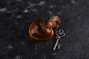 Heart shaped bottle of love potion with small key on black textured table