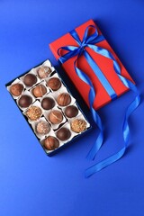 Box with delicious chocolate candies on blue background, flat lay