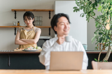 テレワークする夫をキッチンで不機嫌そうに睨む主婦・妻（喧嘩・イライラ・ストレス）  © buritora