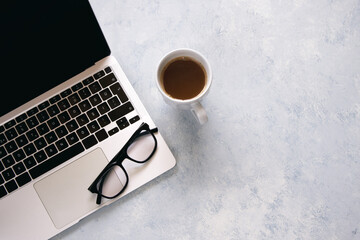 Laptop, cup of coffee and glasses on grey background.