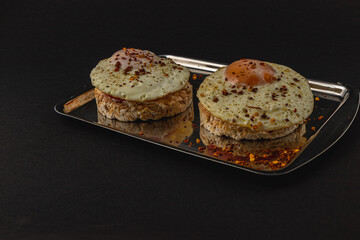 Freshly fried egg on rice bread with tomato and feta cheese on a metal tray