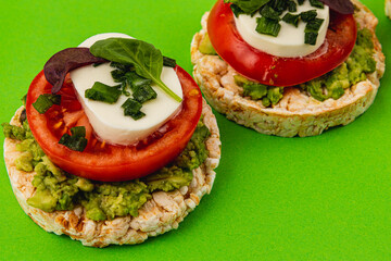 Rice cakes with mozzarella, avocado, spinach and onion on a green background