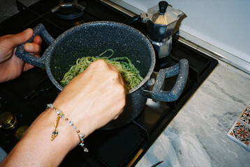 woman mixing pesto pasta in pot on stove top