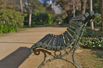 A weathered green wooden bench situated in a peaceful park, surrounded by vegetation and dirt pathways. 