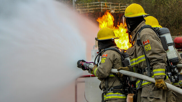 Firefighter Training. Fireman using water and extinguisher for fighting with fire flame in an emergency situation. Under danger situation all firemen wearing fire fighter gear for safety.