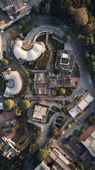 Aerial view of a modern architectural complex nestled amidst lush greenery.  Unique building design and landscaping are showcased from above.