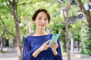 公園でスマホを持つ女性　カメラ目線