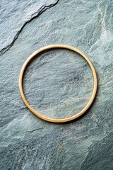A gold bracelet is sitting on a stone surface