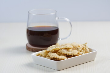 wonton chips in a small white ceramic container on a white table, served with black coffee, with studio lighting