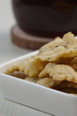 wonton chips in a small white ceramic container on a white table, served with black coffee, with studio lighting