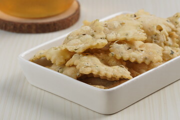 wonton chips in a small white ceramic container on a white table, served with iced tea, with studio lighting
