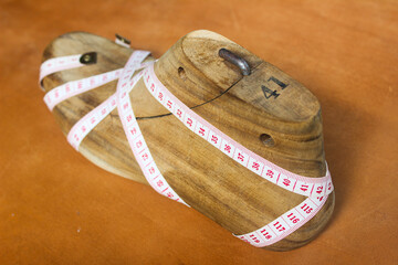 shoe last and measuring tape wrapped around them isolated on brown leather sheet background