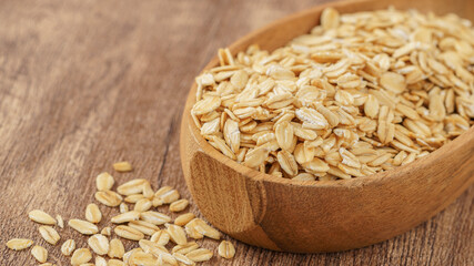 Wooden bowl filled with rolled oats on a rustic wooden surface, perfect for healthy eating and breakfast visuals.