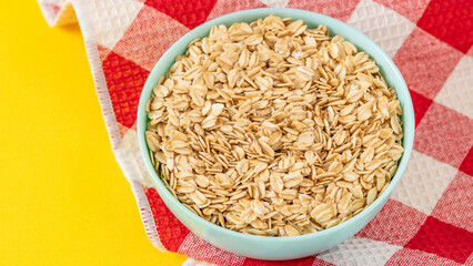 Bowl of rolled oats on a colorful yellow background with a checkered napkin, ideal for healthy breakfast and nutrition concepts.