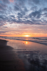 A beautiful sunset casts vibrant colors and reflections on a calm beach, creating a serene and peaceful atmosphere