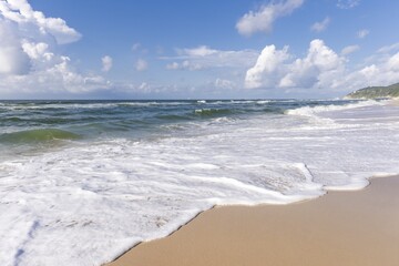Vibrant summer day at the beach with gentle waves lapping on the sandy shore and fluffy clouds in the blue sky