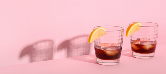 Glasses of rum with ice cubes and lemon slices on pink background