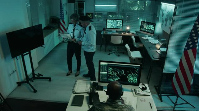 Full high angle CCTV camera footage of multiethnic male and female military officer team working together in operations center, discussing security dossier, analyzing satellite surveillance data