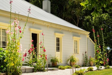 Fototapeta premium Charming white cottage with blooming hollyhocks.