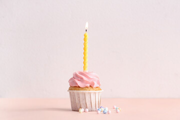 Sweet Birthday cupcake with burning candle and sprinkles on beige background
