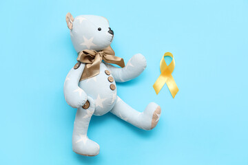 Teddy bear with golden awareness ribbon on color background. International Childhood Cancer Day