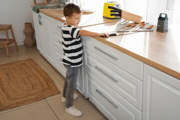 Cute little boy taking knife from counter in kitchen. Child at risk