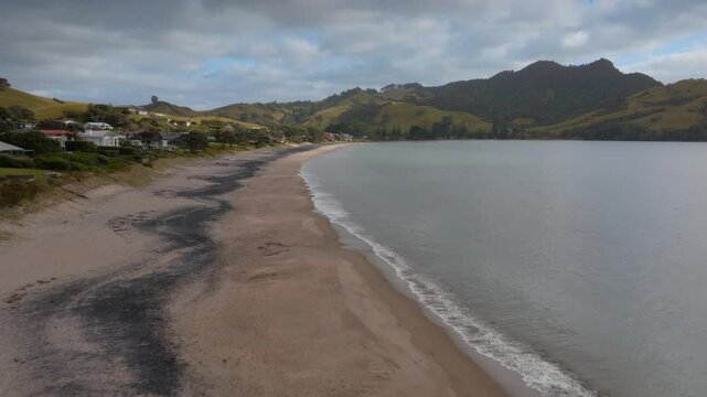 Coastal New Zealand beach scene. Houses line the shore, with calm water and soft sand. Tranquil beauty. SIMPSON BEACH, WHITIANGA, COROMANDEL PENINSULA, NEW ZEALAND