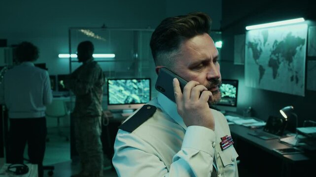 Medium closeup of Caucasian male army lieutenant talking on mobile phone with general chief, while discussing surveillance information and coordinating troop attack or advance