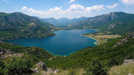 Fototapeta premium Panoramic view of a serene lake surrounded by mountains and lush greenery under a clear blue sky.