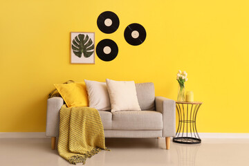 Blanket with pillows on stylish sofa and coffee table near yellow wall