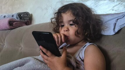 Three Year Old Funny Little Girl Sucking Thumb and Swiping Content on Smartphone