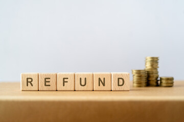 REFUND text on wooden cube block with blurred stack of coins