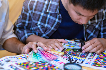 Team graphic designer checking print quality of media graphics proof print and color guides in printing industry. Selected focus