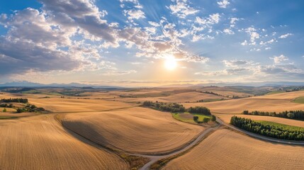 Fototapeta premium A scenic landscape featuring rolling golden fields under a vibrant sky at sunset.