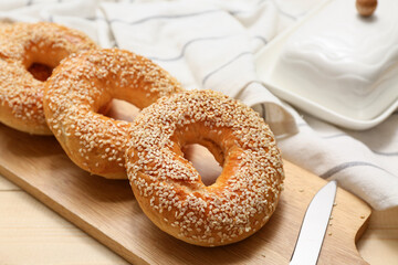 Cutting board of tasty bagels with sesame seeds on wooden background, closeup