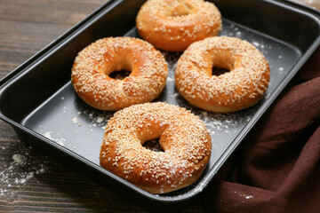 Baking dish of tasty bagels with sesame seeds on wooden background
