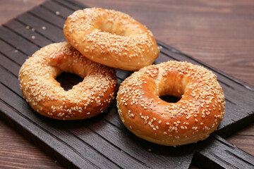 Cutting board of tasty bagels with sesame seeds on wooden background, closeup