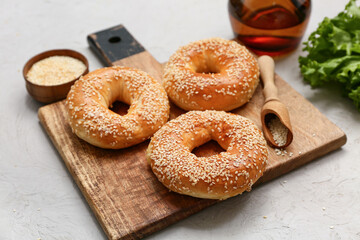 Wooden board of tasty bagels with sesame seeds and fresh lettuce on grey background